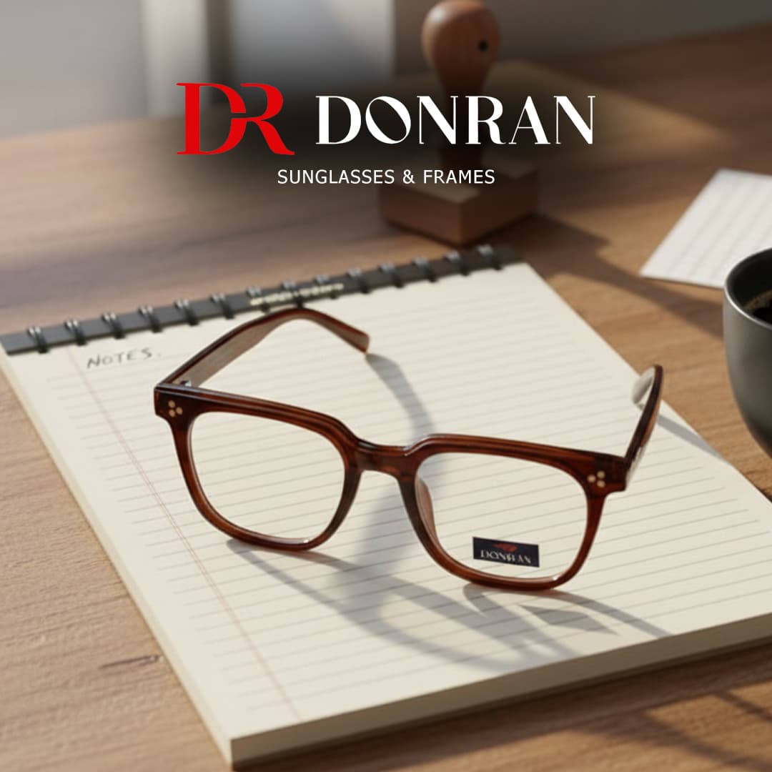 Brown Donran eyeglasses resting on a lined spiral notebook on a sunlit wooden desk.